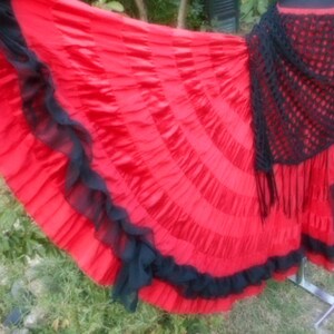 Puede incluir: Una falda roja y negra con volantes y un chal de ganchillo negro. La falda est&aacute; hecha de una tela ligera y tiene una silueta fluida.