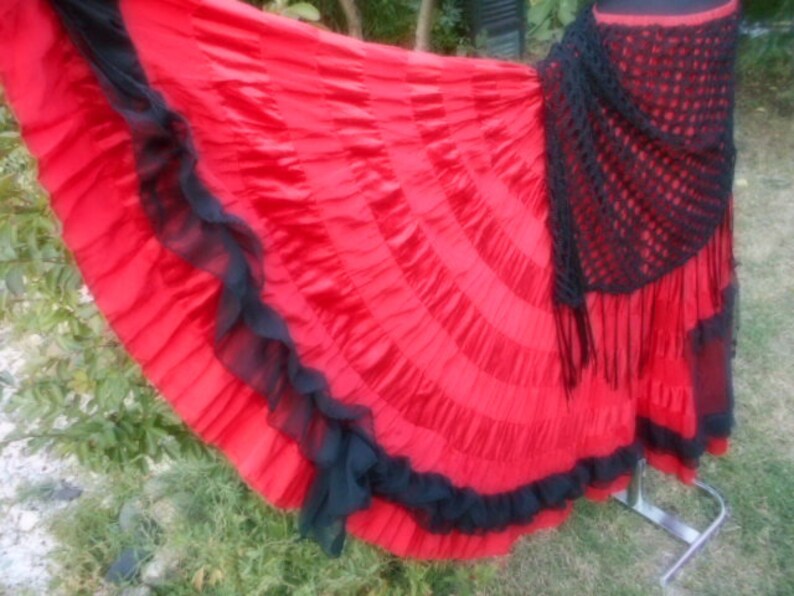 Puede incluir: Una falda roja y negra con volantes y un chal de ganchillo negro. La falda est&aacute; hecha de una tela ligera y tiene una silueta fluida.