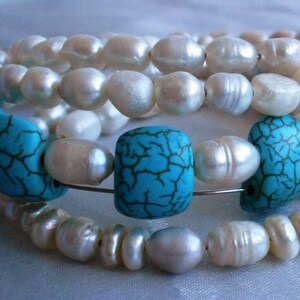 Puede incluir: Un brazalete de perlas multicadena con cuentas turquesa. El brazalete está hecho de perlas blancas y cuentas turquesa con un patrón agrietado.