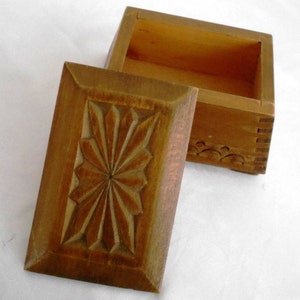 Puede incluir: Una caja de madera con un diseño floral tallado en la tapa. La caja está abierta y el interior está vacío.