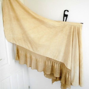May include: A cream-colored tablecloth with a crocheted lace trim. The tablecloth is draped over a table and has a soft, flowing texture.