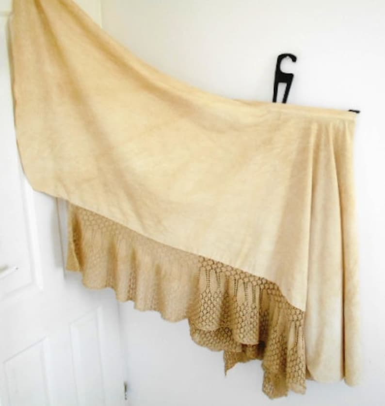 May include: A cream-colored tablecloth with a crocheted lace trim. The tablecloth is draped over a table and has a soft, flowing texture.