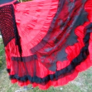 Puede incluir: Una falda roja y negra de varias capas con una cintura de ganchillo. La falda tiene varias capas de encaje negro y tela roja.