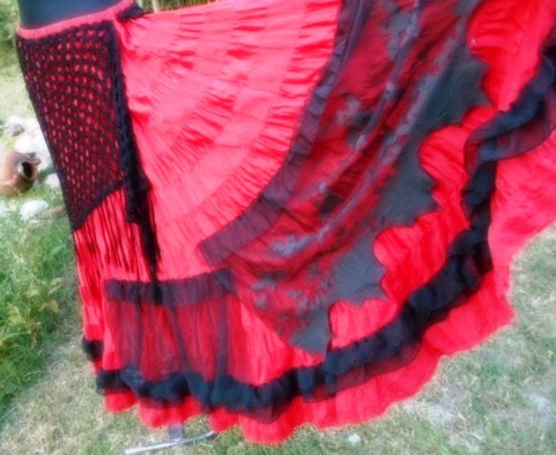 Puede incluir: Una falda roja y negra de varias capas con una cintura de ganchillo. La falda tiene varias capas de encaje negro y tela roja.