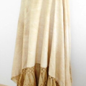 May include: A long, cream-colored skirt with a crocheted lace trim. The skirt is gathered at the waist and falls to the floor.