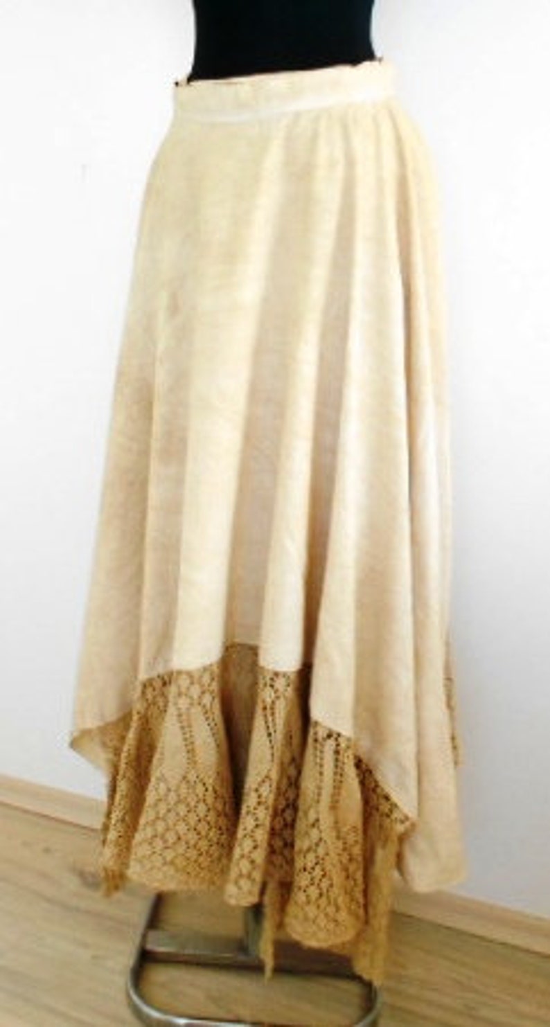 May include: A long, cream-colored skirt with a crocheted lace trim. The skirt is gathered at the waist and falls to the floor.