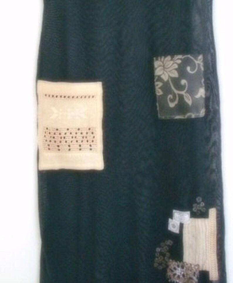 May include: A dark green skirt with a variety of fabric patches sewn on. The patches include a cream-colored square with black embroidery, a floral print fabric patch, and a beige fabric patch with a white design.