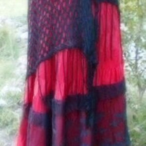 Puede incluir: Una falda roja y negra de capas con una superposici&oacute;n de ganchillo. La falda tiene un dise&ntilde;o de capas con ribete de encaje negro.