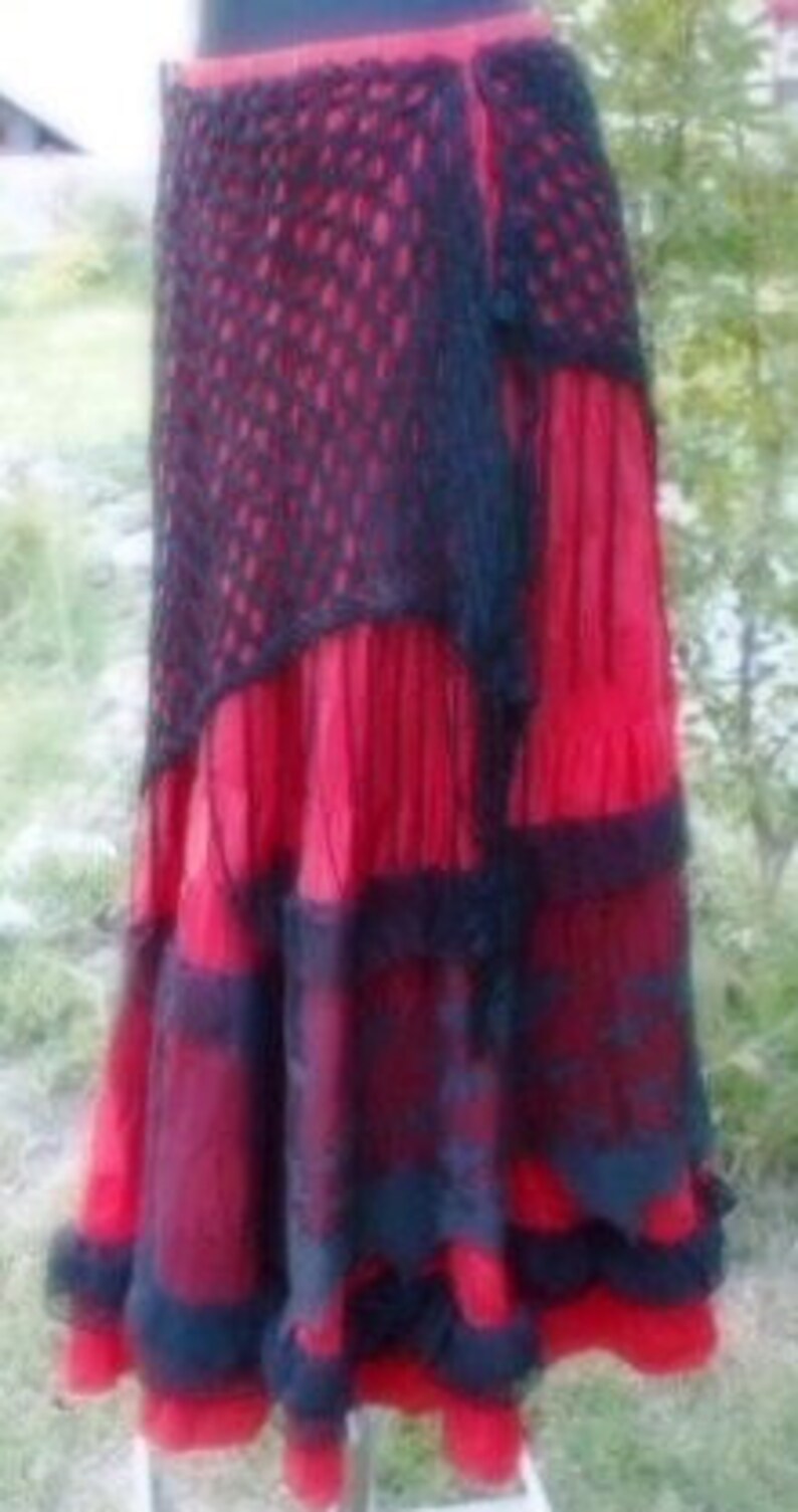 Puede incluir: Una falda roja y negra de capas con una superposici&oacute;n de ganchillo. La falda tiene un dise&ntilde;o de capas con ribete de encaje negro.