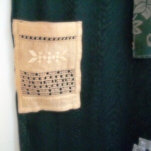 May include: A close-up of a cream-colored crocheted doily with a delicate floral pattern. The doily is attached to a dark green fabric background.