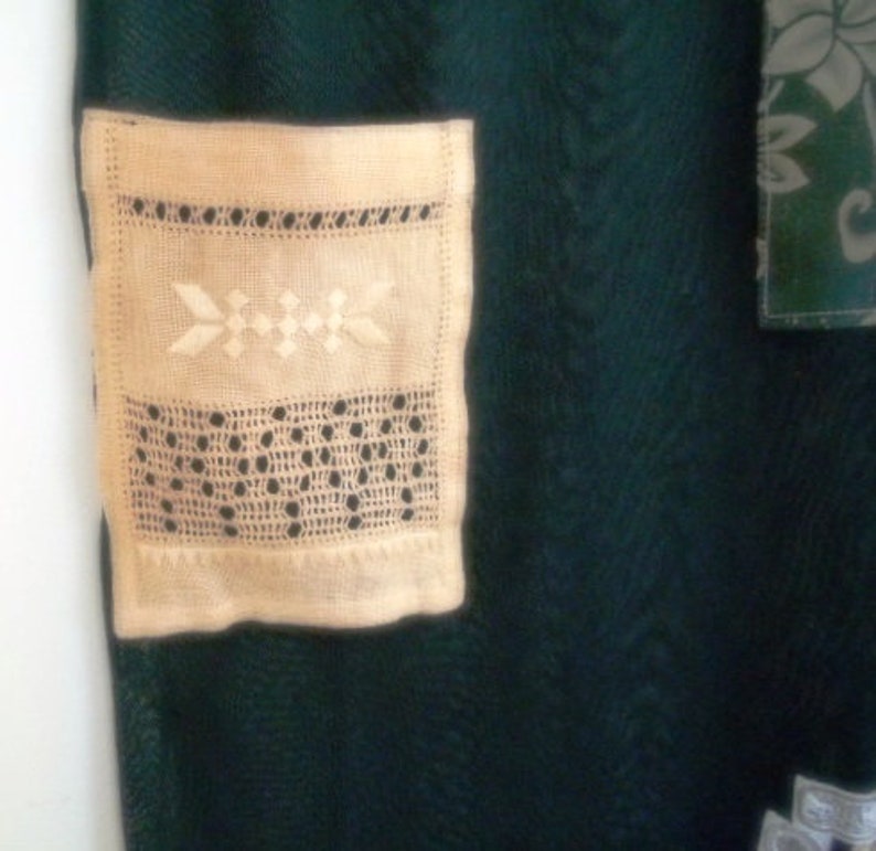 May include: A close-up of a cream-colored crocheted doily with a delicate floral pattern. The doily is attached to a dark green fabric background.
