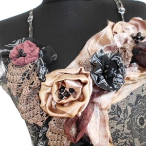Peut inclure: Un corsage en dentelle noire avec un design superposé de fleurs en tissu rose, brun et beige. Les fleurs sont ornées de perles et de paillettes noires.