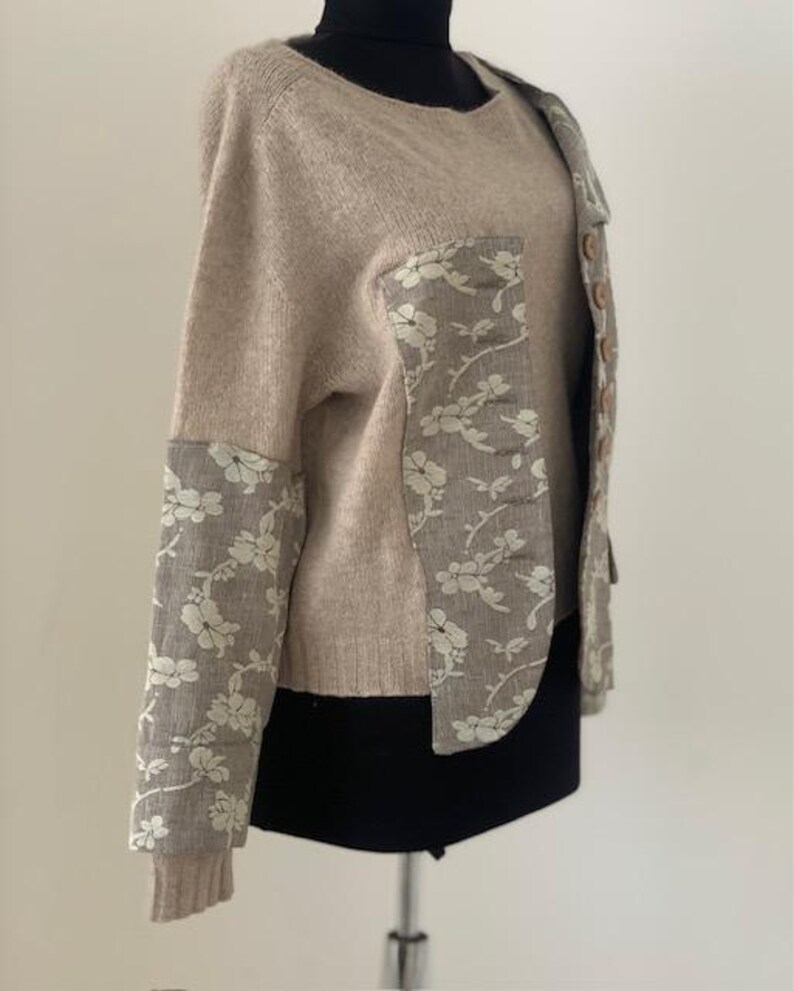 Peut inclure: Un pull en maille beige avec un panneau en tissu &agrave; motif floral sur le devant et les manches. Le pull a un col rond et des manches longues.