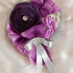 May include: A purple and white fabric flower brooch with a silver ribbon bow.