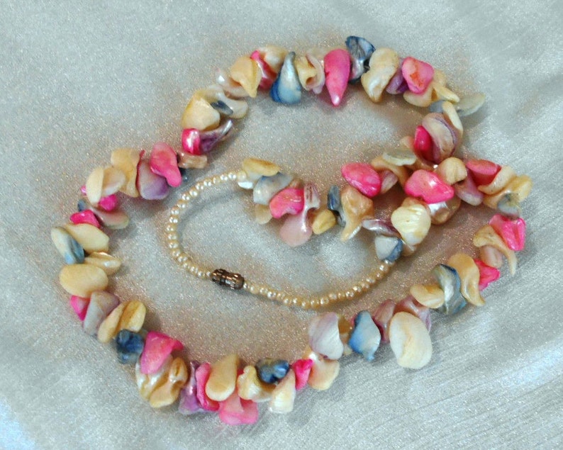 Puede incluir: Un collar de conchas multicolores con conchas rosas, blancas y azules. El collar est&aacute; hecho de conchas de forma irregular y est&aacute; enhebrado en un hilo delgado.