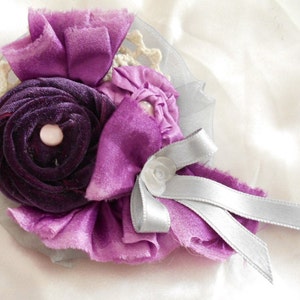 May include: A purple and silver fabric flower brooch with a velvet center. The flower is made of layers of fabric and has a delicate, feminine look.