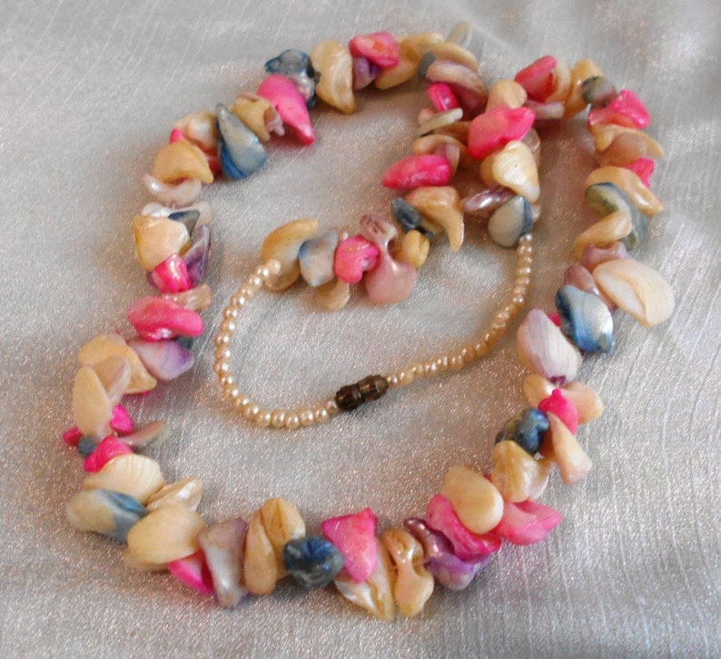 Puede incluir: Un collar de varias hebras hecho de piezas de concha rosa, blanca y azul. El collar est&aacute; enhebrado en una cadena plateada fina y tiene un cierre de broche.