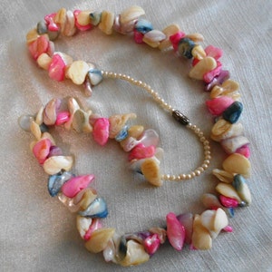 Puede incluir: Un collar de conchas multicolores con conchas rosas, blancas, azules y moradas. El collar est&aacute; hecho de conchas de formas irregulares enhebradas en un hilo delgado.