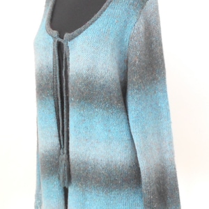 May include: A blue and grey ombre knitted cardigan with a tie at the neck and fringe trim on the sleeves and bottom.