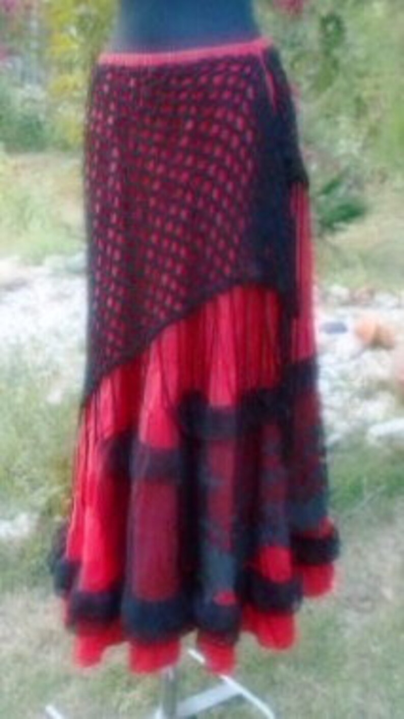 Puede incluir: Una falda roja y negra de varias capas con una superposici&oacute;n de crochet negro. La falda tiene un dobladillo con volantes y est&aacute; hecha de una tela ligera.
