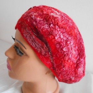 Op de afbeelding: Een rode wollen baret met een textuur en een decoratief ontwerp. De baret is gemaakt van wol en heeft een zacht, comfortabel gevoel.