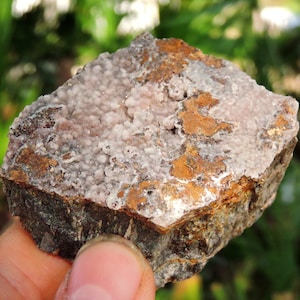 May include: A rough, brown rock with a cluster of small, white, and pink crystals on the surface.