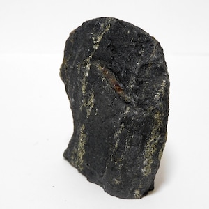 Peut inclure: Un spécimen de pierre rugueuse de couleur gris anthracite foncé avec une texture verticale irrégulière. La surface présente des inclusions minérales métalliques dorées dispersées et une strie allongée brun-rouge incrustée dans la roche.