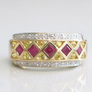 May include: A gold ring with a geometric design. The ring features square, deep red gemstones and smaller yellow gemstones set in a diamond pattern. The top and bottom edges are lined with small, clear gemstones.