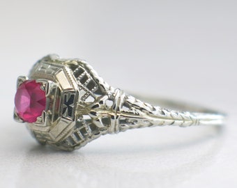 May include: A vintage-style ring with a filigree design and a red gemstone in the center.