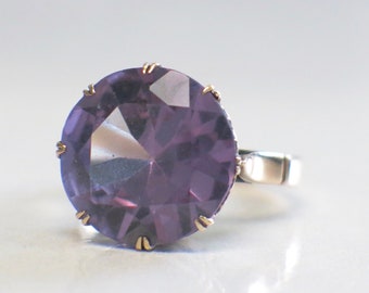 Può includere: Un anello con una grande pietra preziosa sfaccettata di colore viola incastonata in una fascia d'argento.