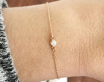 May include: A delicate gold chain bracelet with a single, small, clear gemstone.