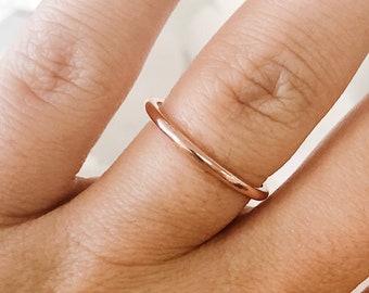 May include: A simple, thin rose gold band ring worn on a finger.