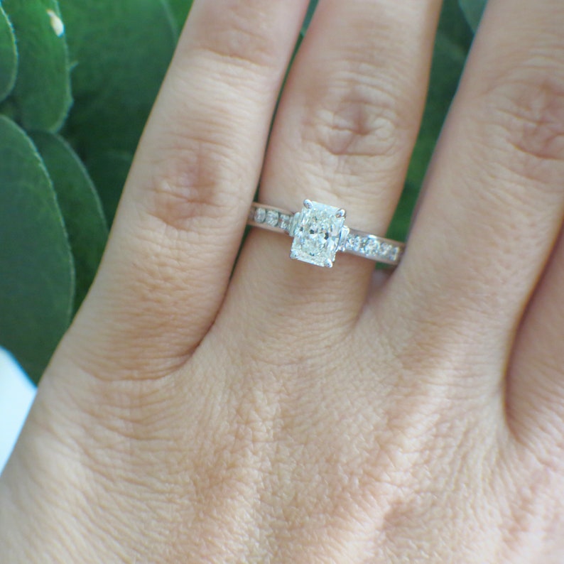 May include: A silver engagement ring with a large, rectangular, clear diamond center stone and smaller diamonds set in a pave band.