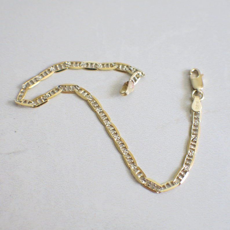 May include: A gold chain bracelet with a mariner link design and small clear stones set into the links. The bracelet has a lobster claw clasp.