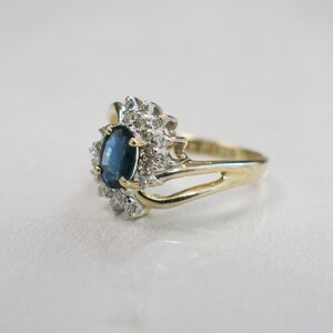 May include: A gold ring with a blue oval sapphire surrounded by smaller diamonds. The ring has a delicate, twisted band.