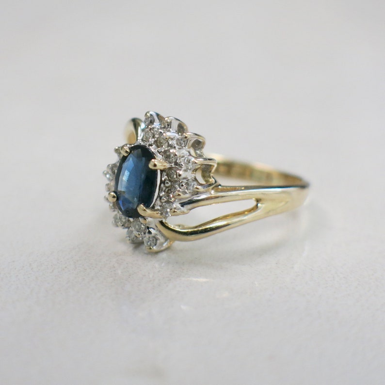 May include: A gold ring with a blue oval sapphire surrounded by smaller diamonds. The ring has a delicate, twisted band.