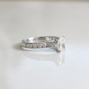 May include: A silver engagement ring with a large, clear, cushion-cut diamond and a band of smaller diamonds.