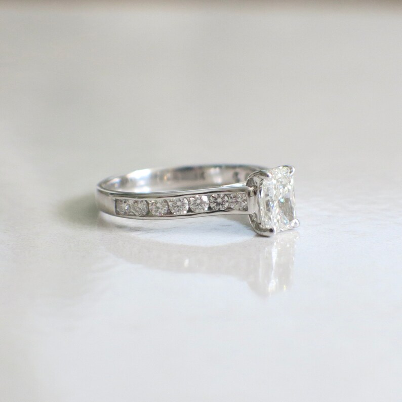May include: A silver engagement ring with a large, clear, cushion-cut diamond and a band of smaller diamonds.