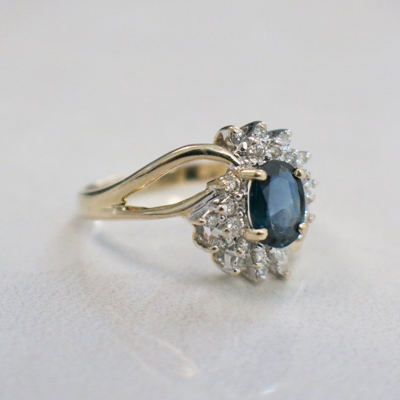 May include: A gold ring with a large oval-shaped blue sapphire surrounded by smaller diamonds.