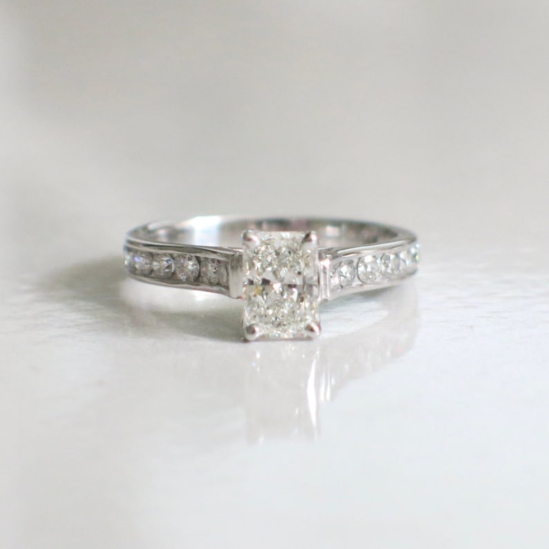 May include: A silver engagement ring with a large, rectangular, clear diamond center stone and a band of smaller diamonds.