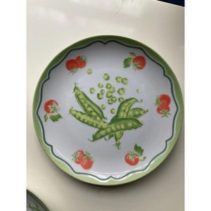 May include: A white ceramic plate with a green scalloped edge features a design of green peas and red tomatoes.