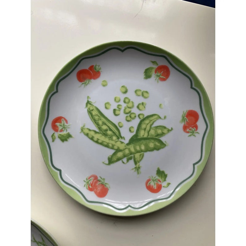 May include: A white ceramic plate with a green scalloped edge features a design of green peas and red tomatoes.