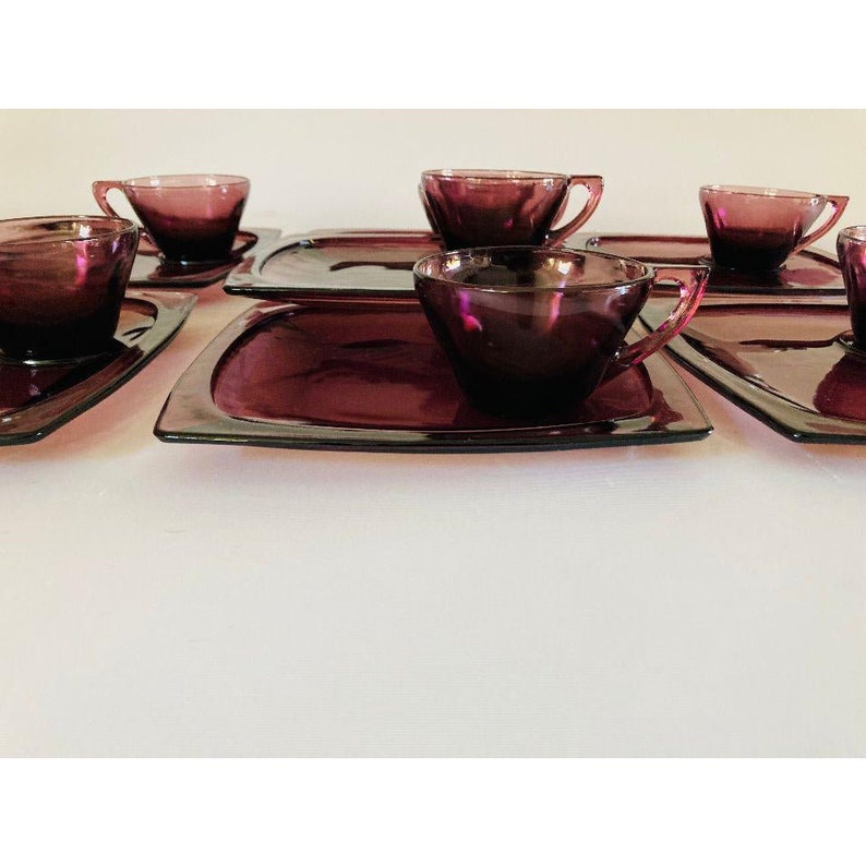 May include: Set of six amethyst glass cups and saucers. The cups and saucers have a square shape with rounded edges.