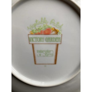 May include: White ceramic plate with a green and brown illustration of a pot with vegetables and the text "Vegetable Patch Victory Garden" and "Tastemaker Sonoma".