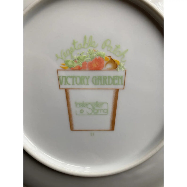 May include: White ceramic plate with a green and brown illustration of a pot with vegetables and the text "Vegetable Patch Victory Garden" and "Tastemaker Sonoma".