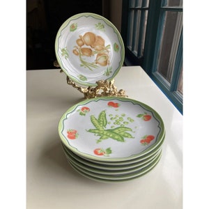 May include: Set of six white ceramic dinner plates with a green rim. The plates feature a green and red vegetable design.