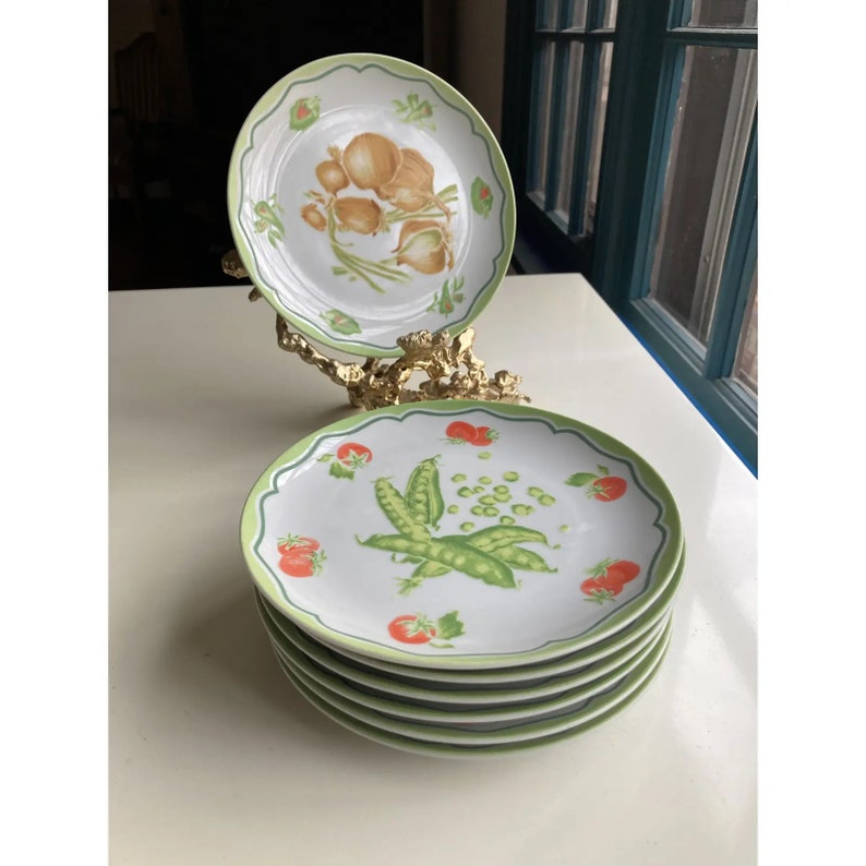 May include: Set of six white ceramic dinner plates with a green rim. The plates feature a green and red vegetable design.