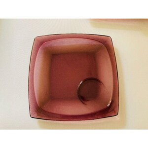 May include: A square, amethyst-colored glass dish with a rounded inner rim and a small, circular indentation in the center.