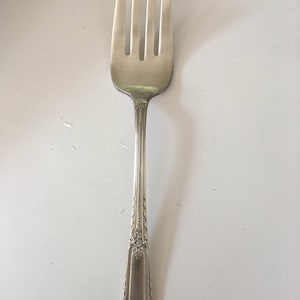 May include: A silver fork with a decorative handle. The fork has four tines and a long, slender handle with an ornate design.