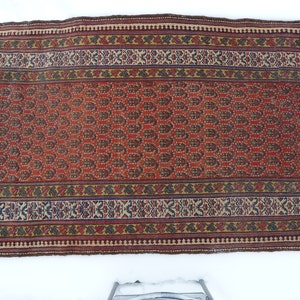 May include: A red, brown, and cream colored rug with a paisley pattern. The rug has a border with a geometric design.